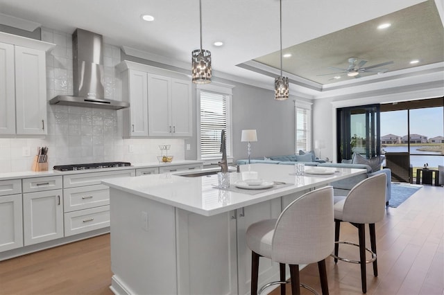 kitchen with pendant lighting, a center island with sink, wall chimney exhaust hood, and a healthy amount of sunlight