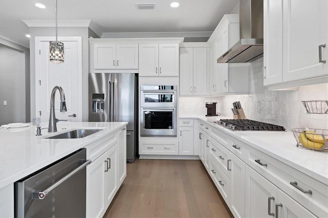 kitchen with stainless steel appliances, wall chimney range hood, wood-type flooring, decorative light fixtures, and white cabinets