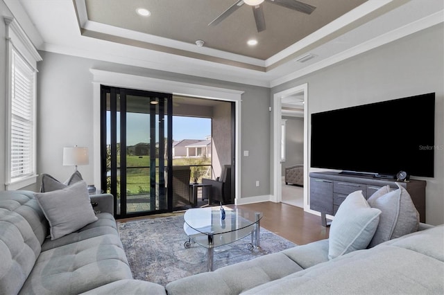 living room with a tray ceiling, ceiling fan, crown molding, and hardwood / wood-style flooring