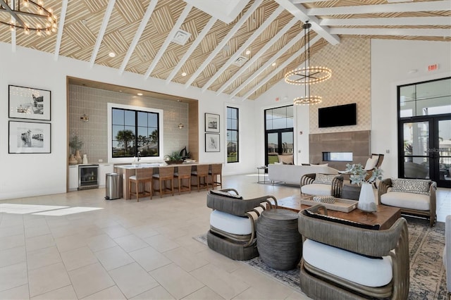 living room with a tile fireplace, high vaulted ceiling, an inviting chandelier, wine cooler, and beamed ceiling