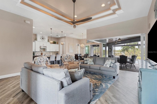 living room featuring light wood-type flooring, a raised ceiling, ceiling fan, and crown molding