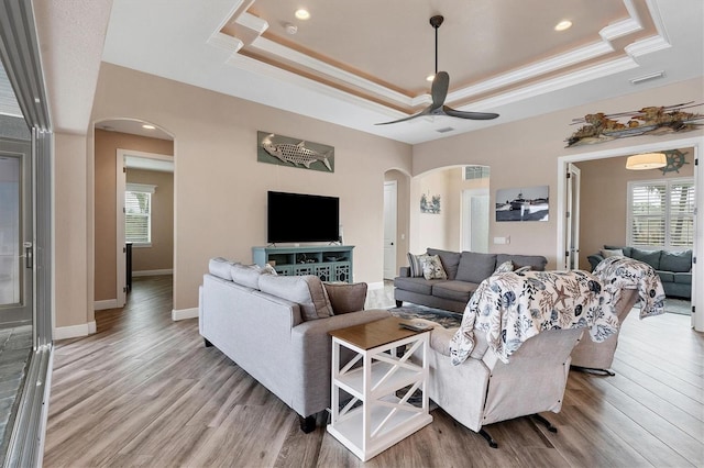 living room with a raised ceiling, light hardwood / wood-style flooring, ceiling fan, and crown molding