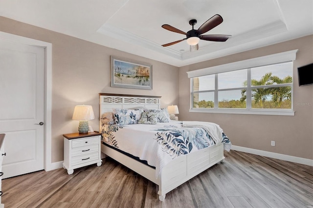 bedroom featuring light hardwood / wood-style flooring, a raised ceiling, ceiling fan, and ornamental molding