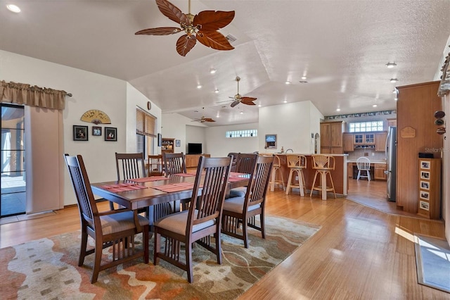 dining space featuring a textured ceiling, ceiling fan, light hardwood / wood-style floors, and lofted ceiling