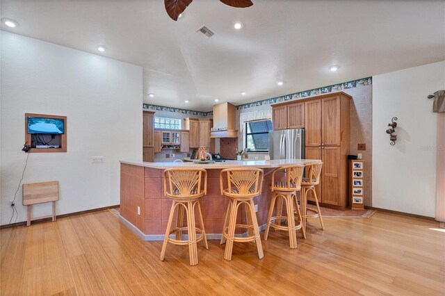 kitchen with kitchen peninsula, stainless steel fridge, light hardwood / wood-style floors, and a breakfast bar area