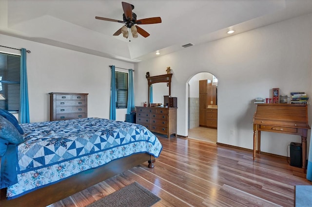 bedroom featuring a raised ceiling, connected bathroom, ceiling fan, and wood-type flooring