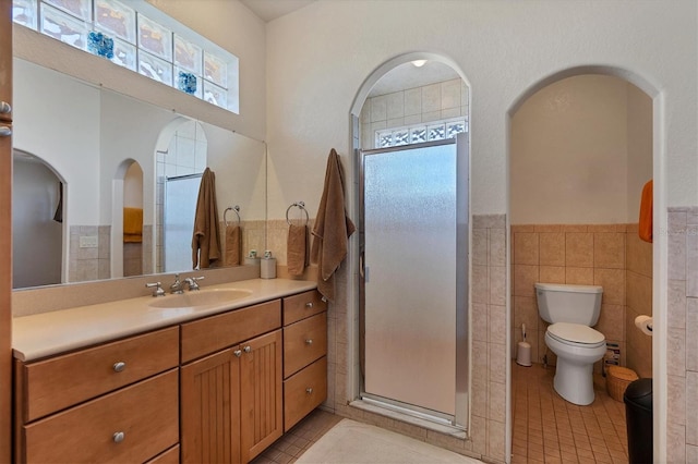 bathroom with vanity, a shower with door, tile patterned flooring, toilet, and tile walls