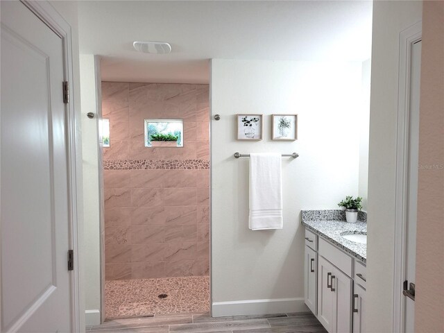 bathroom featuring wood finished floors, visible vents, vanity, baseboards, and a tile shower