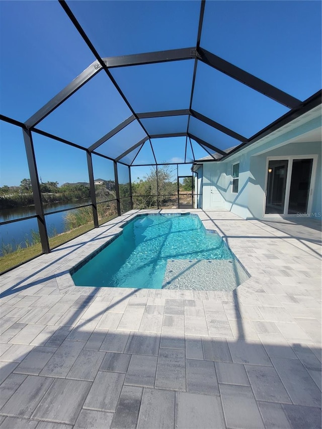 pool featuring glass enclosure, a patio area, and a water view