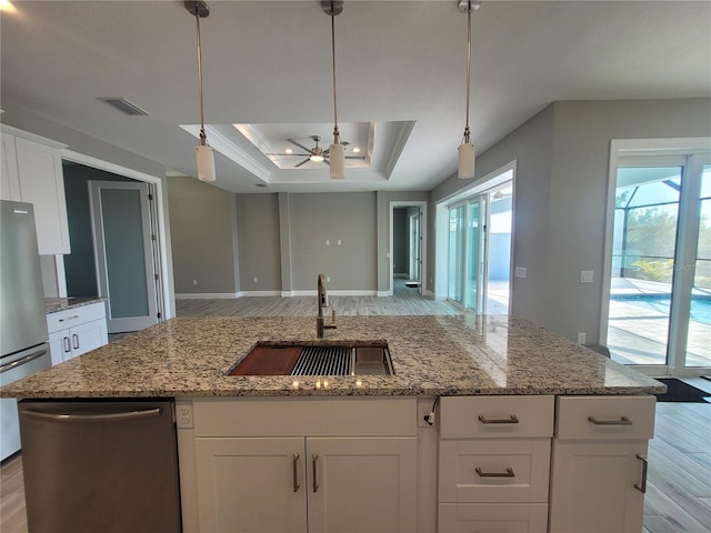 kitchen with a tray ceiling, visible vents, appliances with stainless steel finishes, open floor plan, and a sink