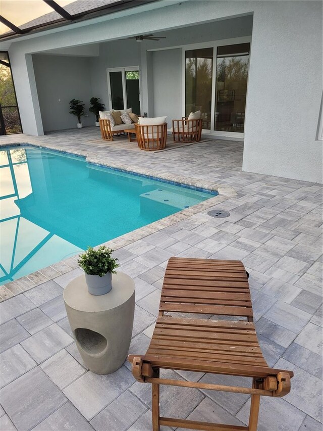 pool with ceiling fan, glass enclosure, a patio area, and an outdoor living space