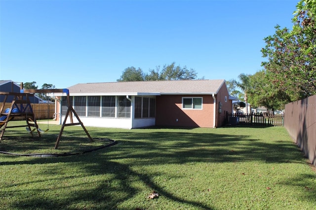 rear view of property with a sunroom, a playground, and a lawn