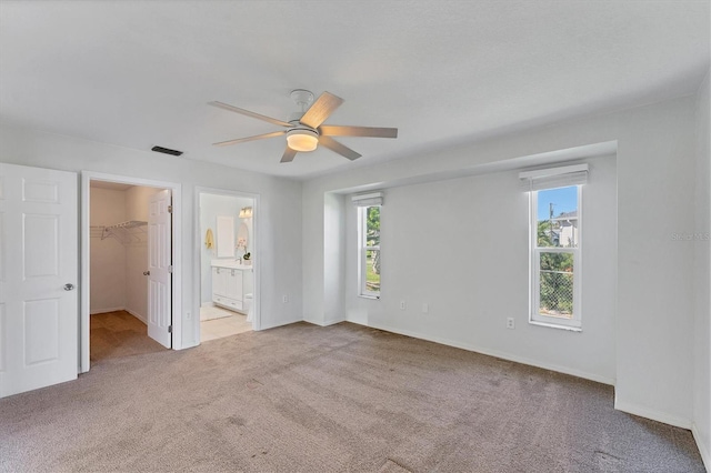 unfurnished bedroom featuring light carpet, a walk in closet, ceiling fan, connected bathroom, and a closet