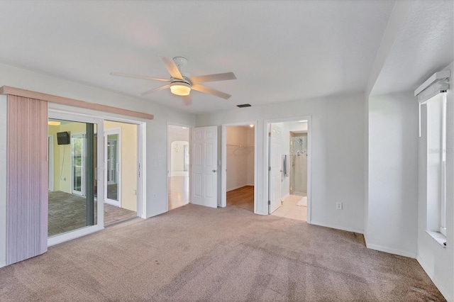 unfurnished bedroom with a spacious closet, a closet, ceiling fan, and light carpet