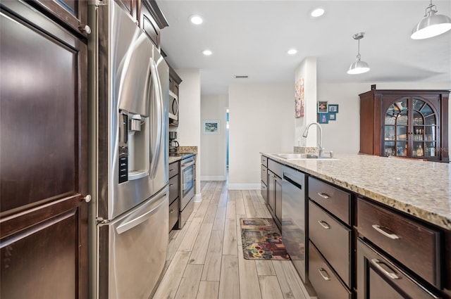 kitchen with sink, stainless steel appliances, light stone counters, light hardwood / wood-style flooring, and decorative light fixtures