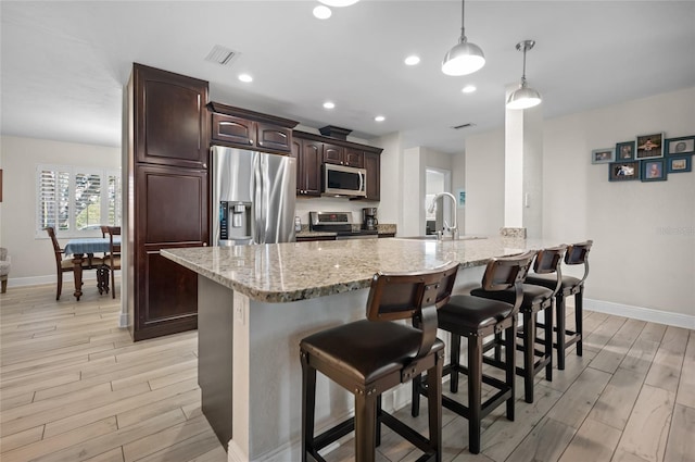 kitchen with hanging light fixtures, dark brown cabinetry, light wood-type flooring, appliances with stainless steel finishes, and kitchen peninsula