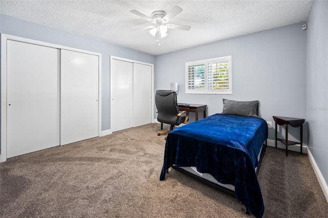 bedroom featuring a textured ceiling, ceiling fan, dark carpet, and two closets