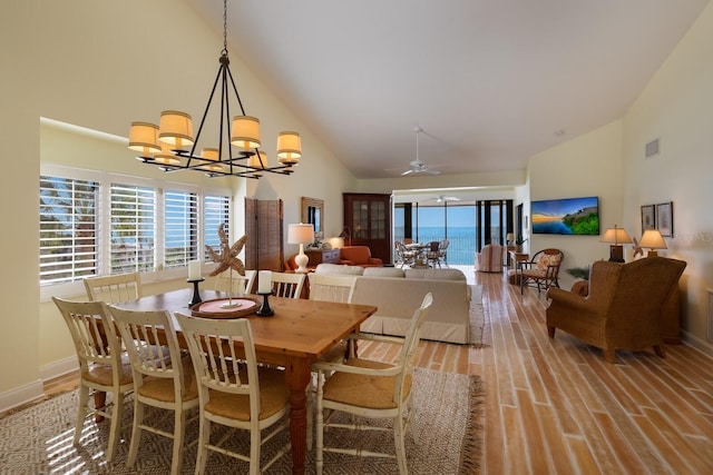 dining space featuring high vaulted ceiling, ceiling fan with notable chandelier, and light wood-type flooring