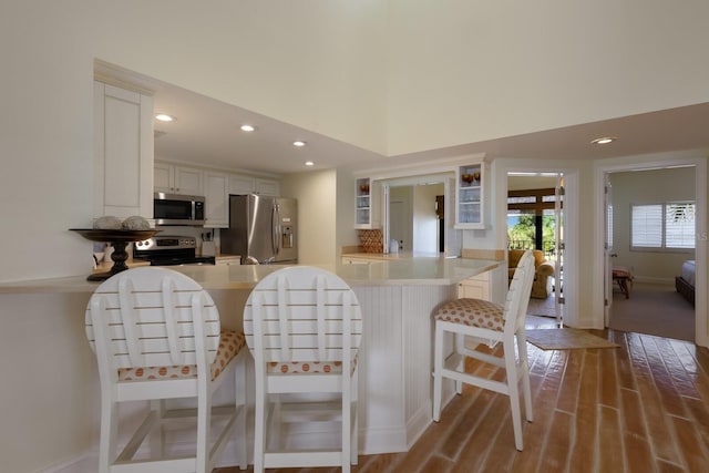 kitchen featuring a breakfast bar, kitchen peninsula, a towering ceiling, white cabinetry, and stainless steel appliances