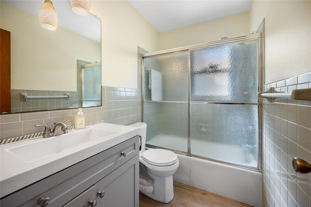 full bathroom with tile walls, hardwood / wood-style floors, bath / shower combo with glass door, vanity, and toilet