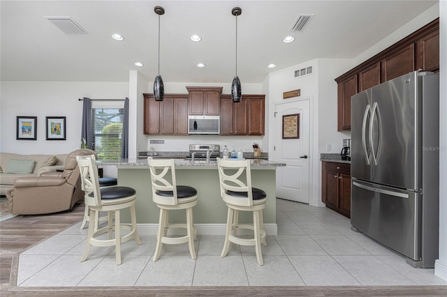 kitchen with pendant lighting, a kitchen bar, a kitchen island with sink, light stone counters, and stainless steel appliances