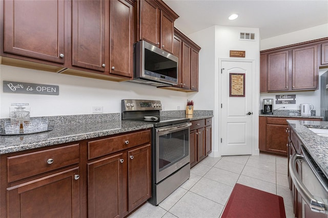 kitchen featuring appliances with stainless steel finishes, light tile patterned floors, and dark stone countertops