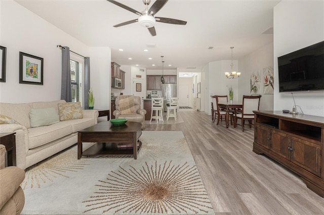 living room featuring ceiling fan with notable chandelier and light hardwood / wood-style floors