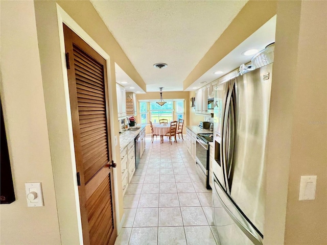 kitchen featuring white cabinetry, sink, stainless steel appliances, decorative light fixtures, and light tile patterned floors