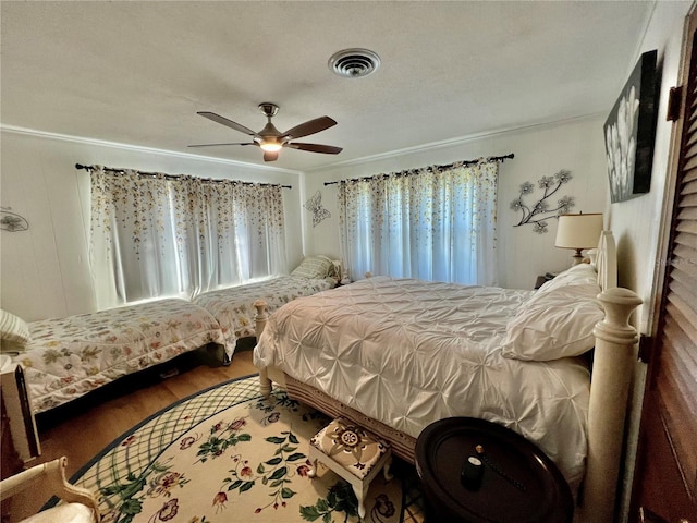 bedroom with ceiling fan, wood walls, hardwood / wood-style floors, a textured ceiling, and ornamental molding