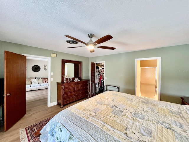 bedroom with a spacious closet, ceiling fan, a textured ceiling, a closet, and light wood-type flooring