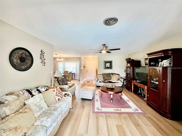 living room featuring light hardwood / wood-style flooring, ceiling fan with notable chandelier, and a textured ceiling