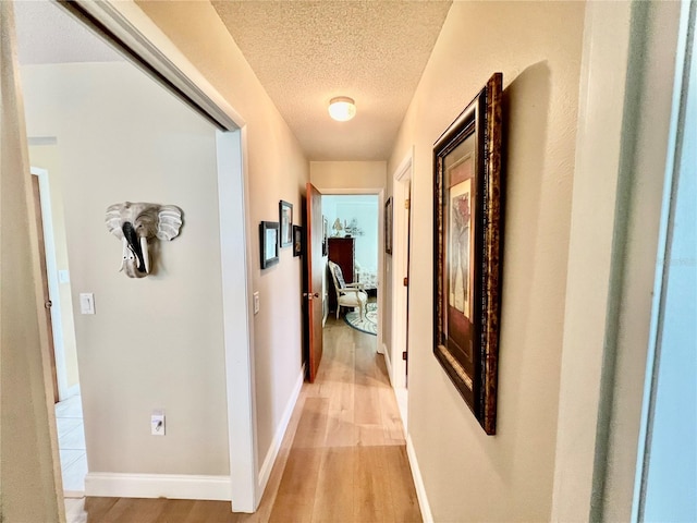 hall with a textured ceiling and light hardwood / wood-style flooring