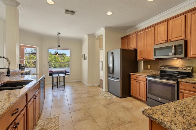 kitchen featuring light stone counters, stainless steel appliances, crown molding, sink, and hanging light fixtures