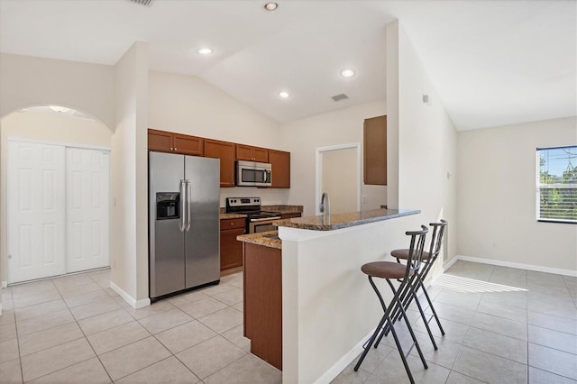 kitchen featuring a breakfast bar, lofted ceiling, dark stone countertops, appliances with stainless steel finishes, and kitchen peninsula