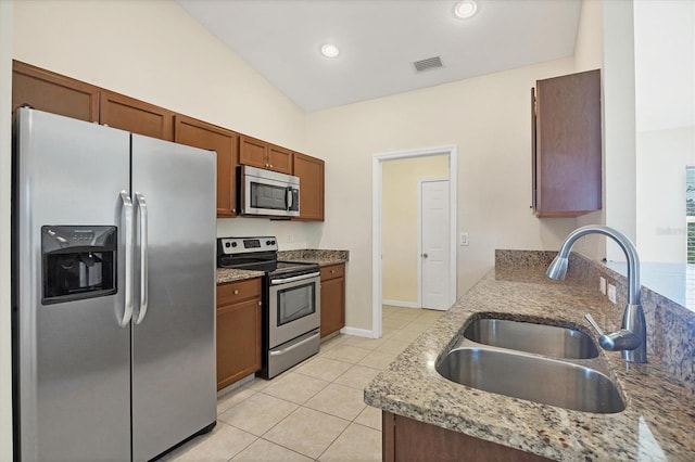 kitchen featuring sink, light stone counters, vaulted ceiling, light tile patterned floors, and appliances with stainless steel finishes