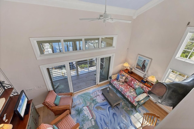 living room with wood-type flooring, a towering ceiling, ceiling fan, and crown molding