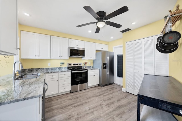 kitchen with sink, light wood-type flooring, light stone countertops, appliances with stainless steel finishes, and white cabinetry