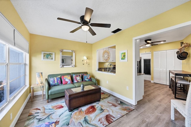 living room with ceiling fan, light hardwood / wood-style flooring, a textured ceiling, and sink