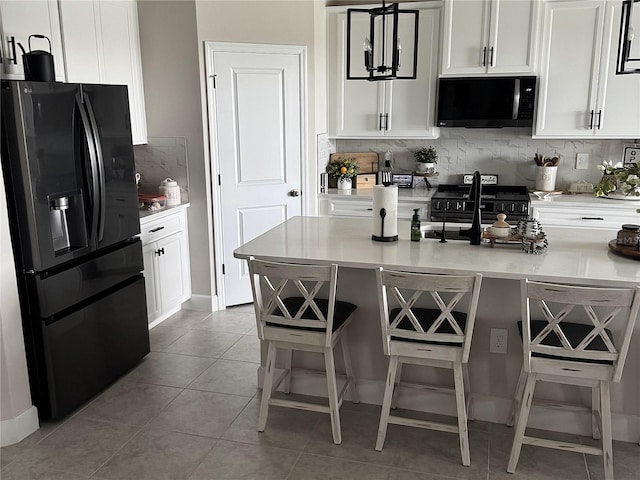 kitchen with backsplash, black appliances, light tile patterned floors, white cabinetry, and a breakfast bar area