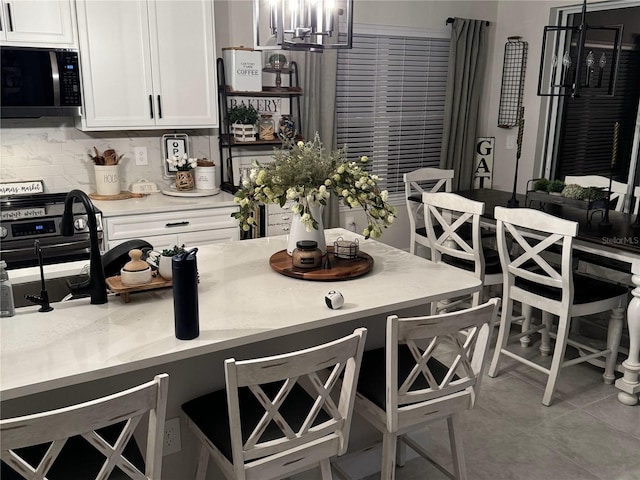 kitchen with white cabinets, decorative backsplash, light tile patterned floors, and a breakfast bar