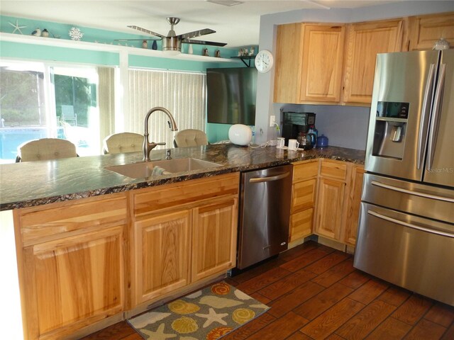 kitchen featuring kitchen peninsula, stainless steel appliances, sink, dark stone countertops, and dark hardwood / wood-style floors