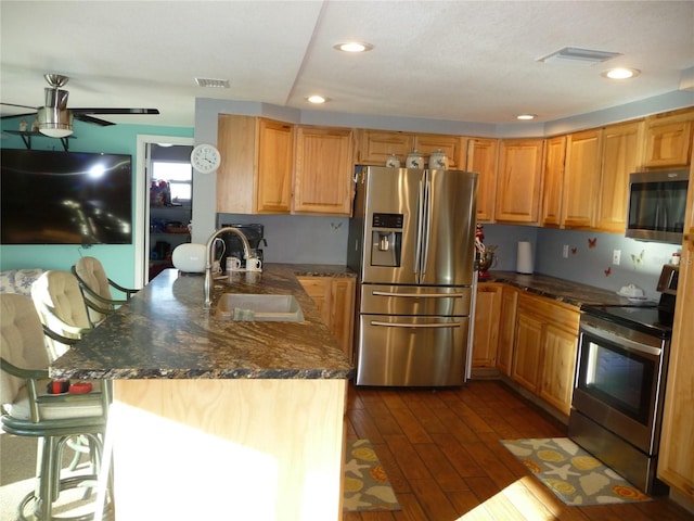 kitchen featuring ceiling fan, sink, dark hardwood / wood-style floors, a kitchen bar, and appliances with stainless steel finishes