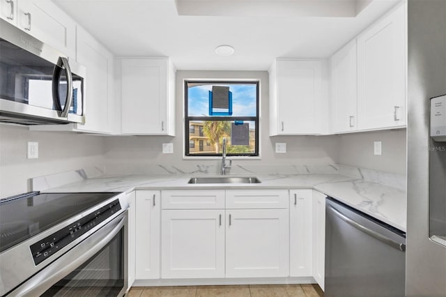 kitchen featuring white cabinetry, sink, light stone countertops, light tile patterned flooring, and appliances with stainless steel finishes