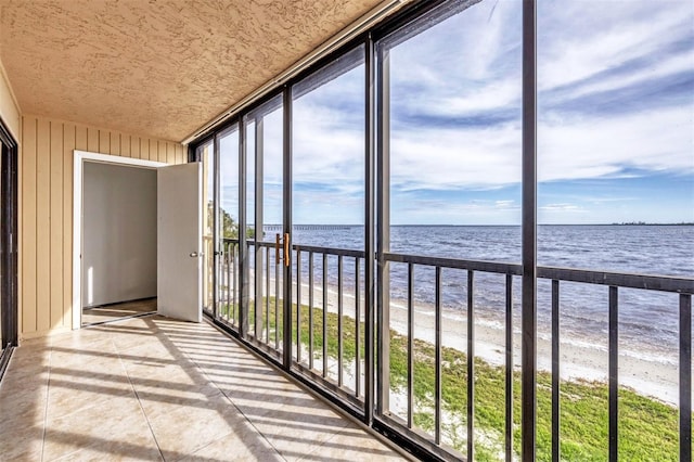 unfurnished sunroom featuring a water view and a beach view