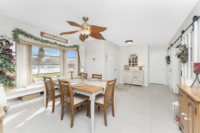 dining space with a barn door, ceiling fan, and a textured ceiling