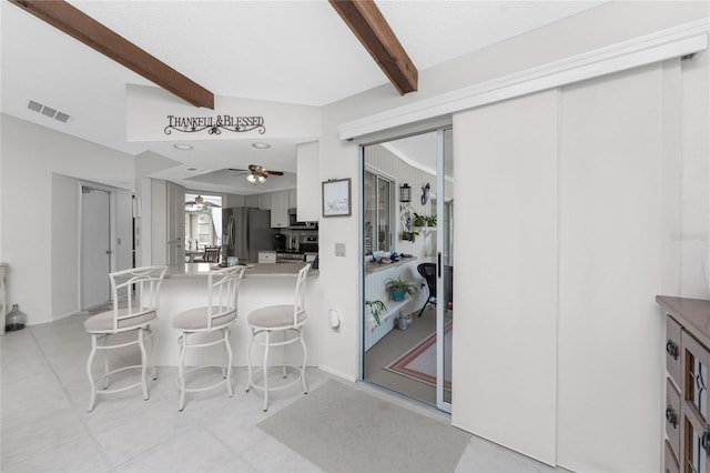 kitchen with kitchen peninsula, a kitchen breakfast bar, ceiling fan, beam ceiling, and stainless steel refrigerator