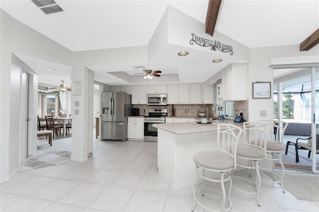 kitchen with stainless steel appliances, kitchen peninsula, a tray ceiling, a breakfast bar area, and white cabinets