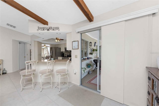 kitchen featuring white cabinetry, ceiling fan, beamed ceiling, stainless steel fridge, and a breakfast bar area