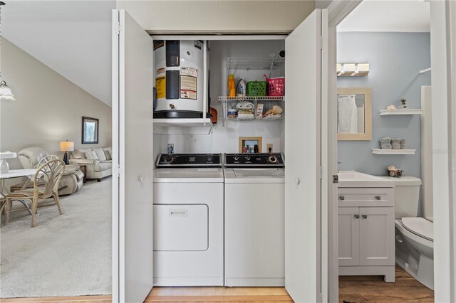 clothes washing area with separate washer and dryer, water heater, and light hardwood / wood-style flooring