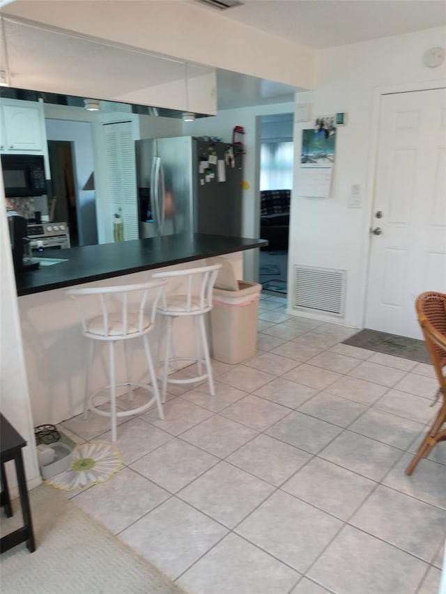 kitchen featuring white cabinets, white range oven, light tile patterned floors, and a breakfast bar area